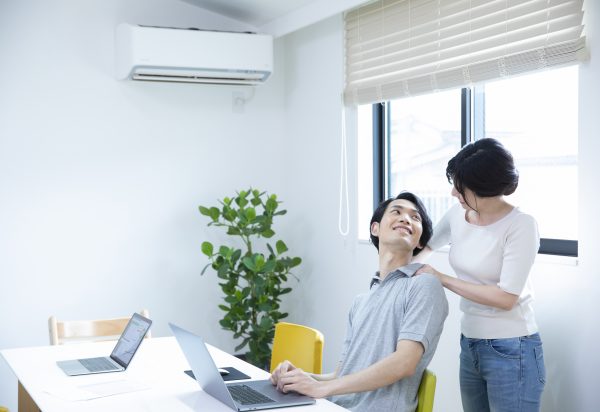 疲れた旦那の肩をマッサージする女性